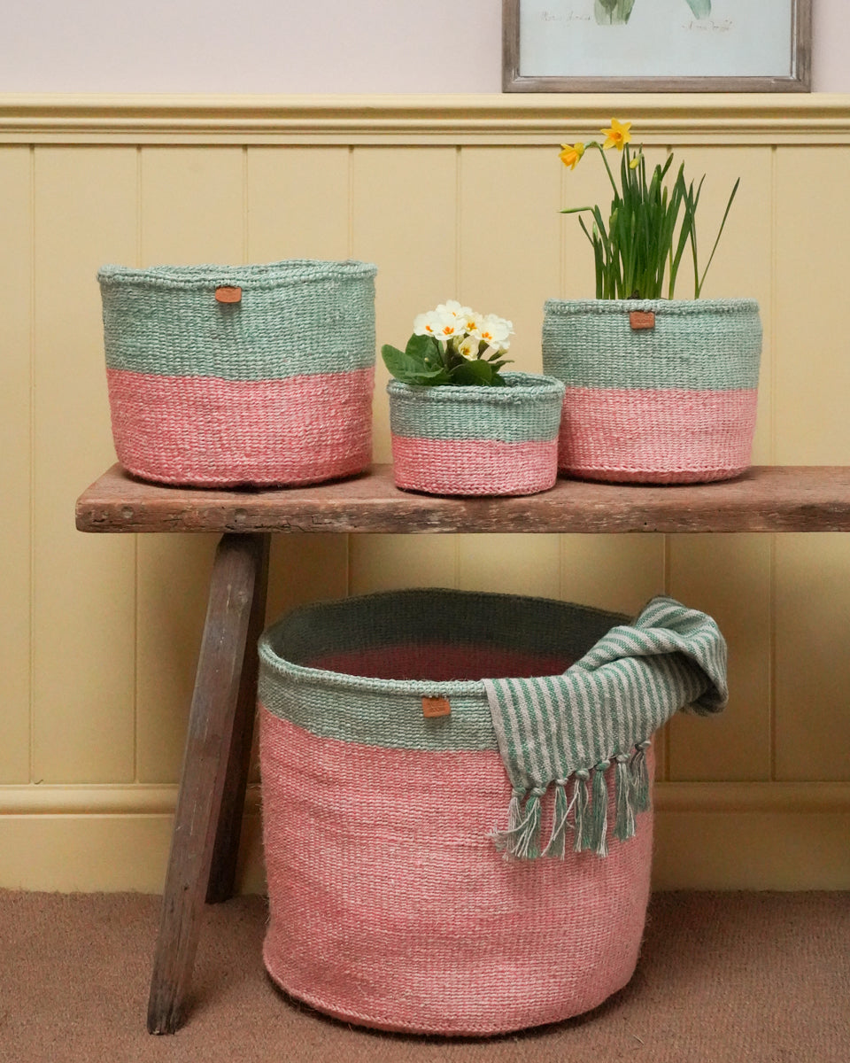 Set of woven baskets in pink and green on a wooden table against a yellow wall.