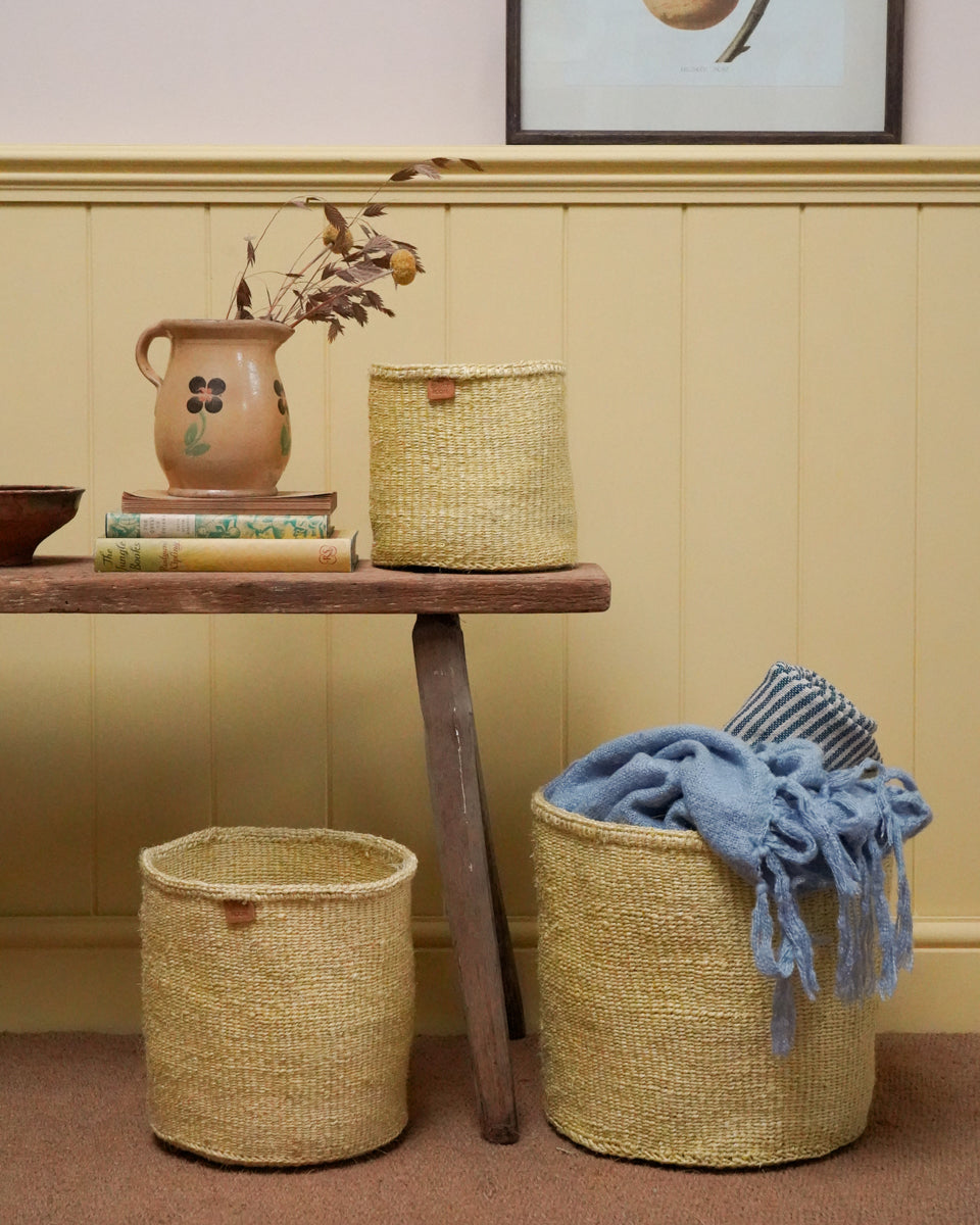 Woven yellow baskets with a blue blanket on a wooden table against a yellow wall.