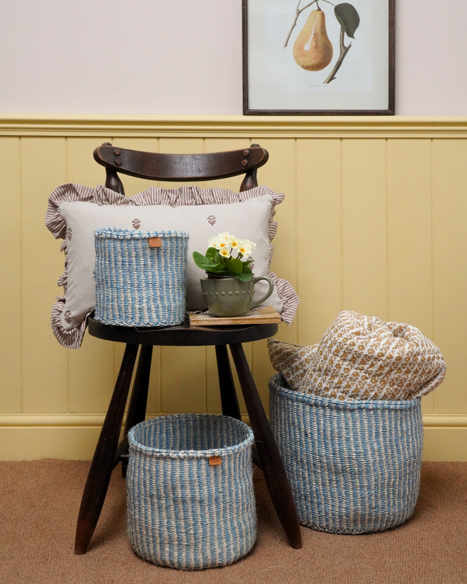 Woven baskets and a cushion on a wooden stool against a wall with a framed picture.