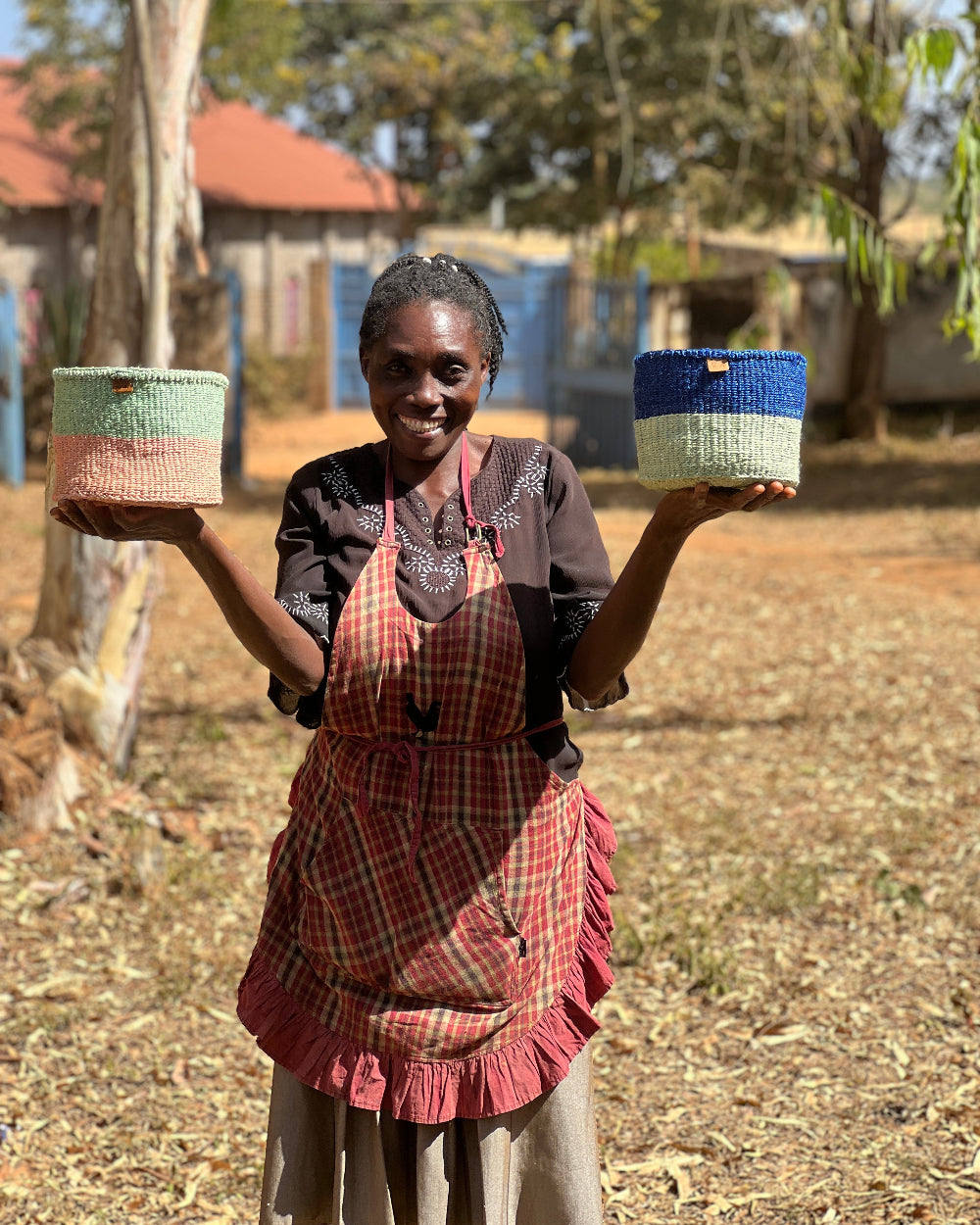 Woman holding two colorful woven baskets in a rural setting