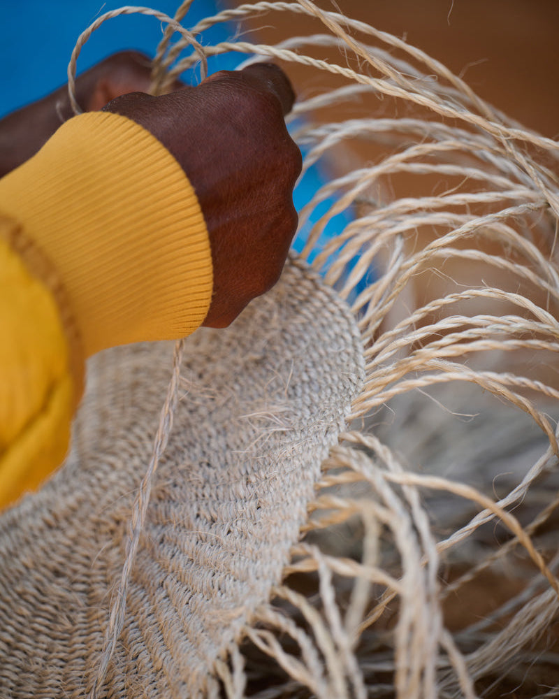 Female basket weaver wearing a yellow sleeve holding a woven basket with dried grasses.