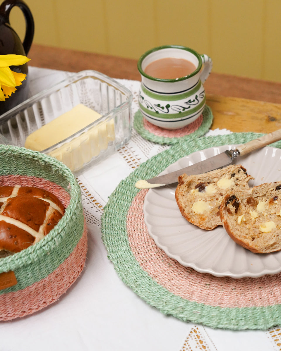 Woven pink and green placmat with a plate of hot cross buns