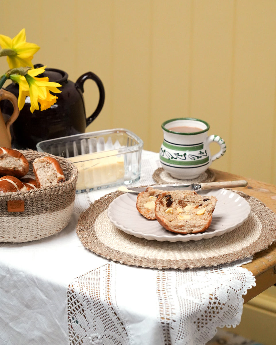 Tea time setting with bread, tea cup, and teapot on a table. Woven placemat, bread basket and coaster.