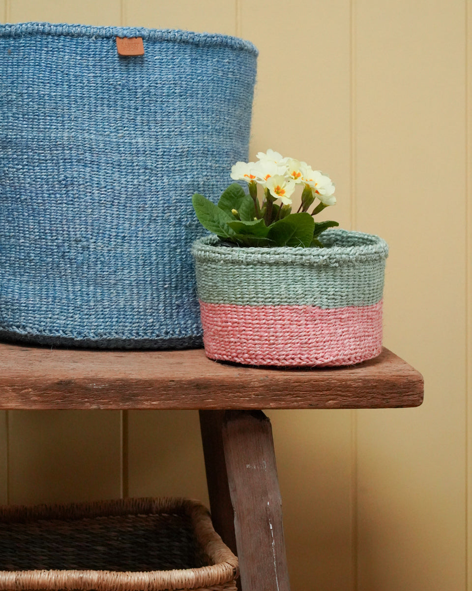 Woven baskets with a plant on a wooden surface against a beige wall.