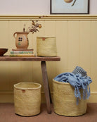 Woven yellow baskets with a blue blanket on a wooden table against a yellow wall.