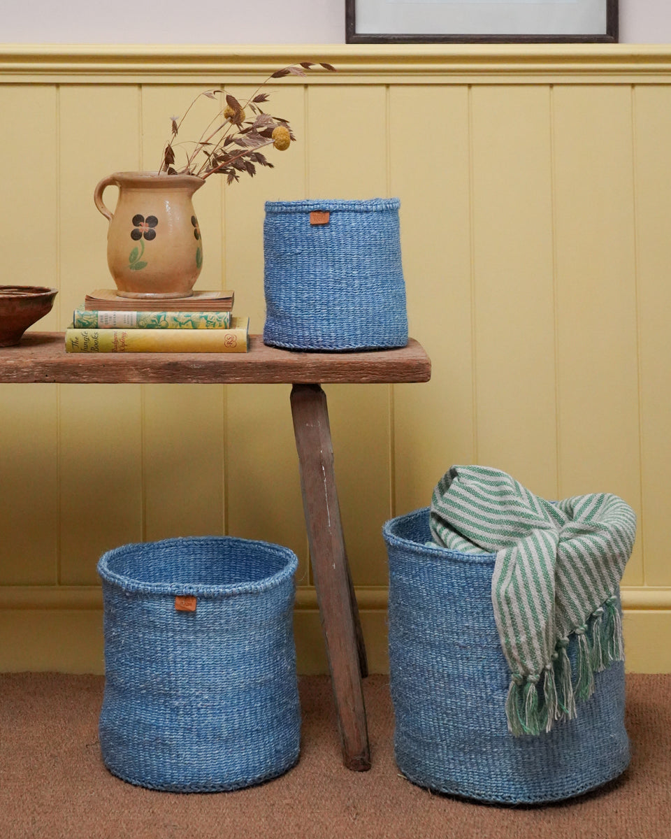 Blue woven baskets with a striped blanket on a wooden table against a yellow wall.
