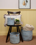 Woven baskets and a cushion on a wooden stool against a wall with a framed picture.