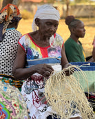 Woman sitting and working with a woven basket in an outdoor setting