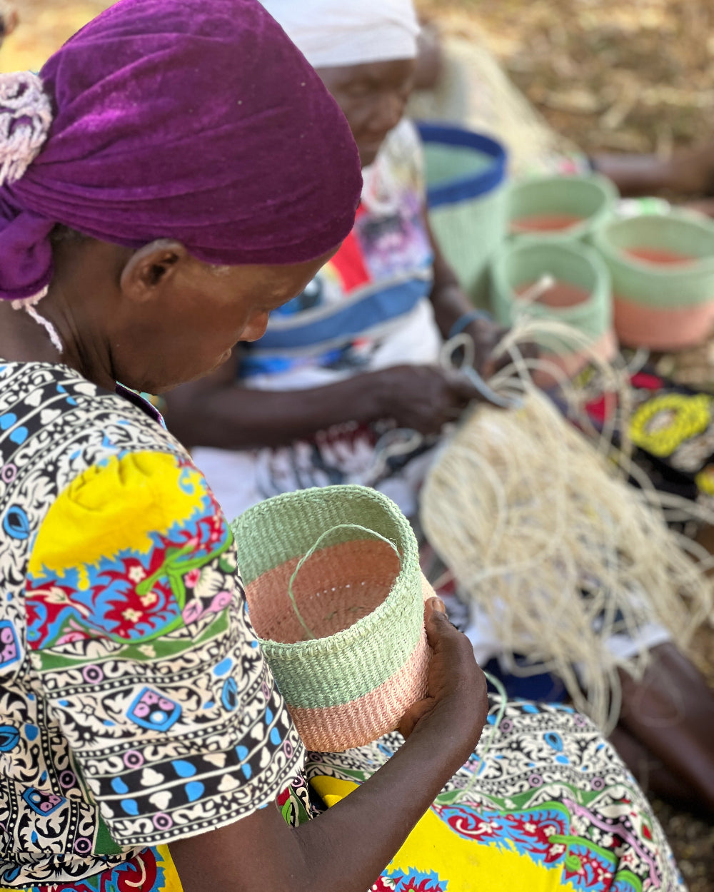 Woman in colorful traditional attire holding a woven basket in a natural setting.
