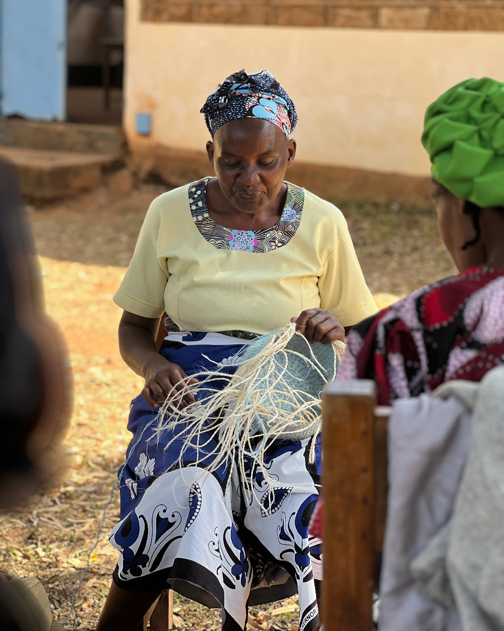 Kenyan Woman in traditional attire weaving a sisal basket outdoors