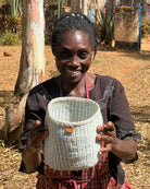 Woman holding a woven basket outdoors with trees and a wall in the background