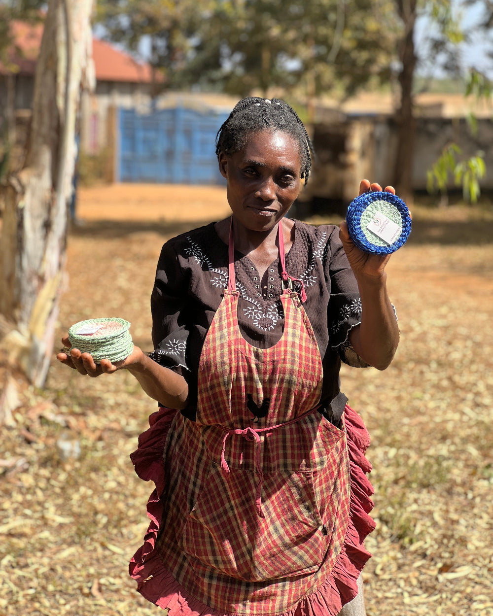 Woman holding two blue and white coasters outdoors with trees and a building in the background.