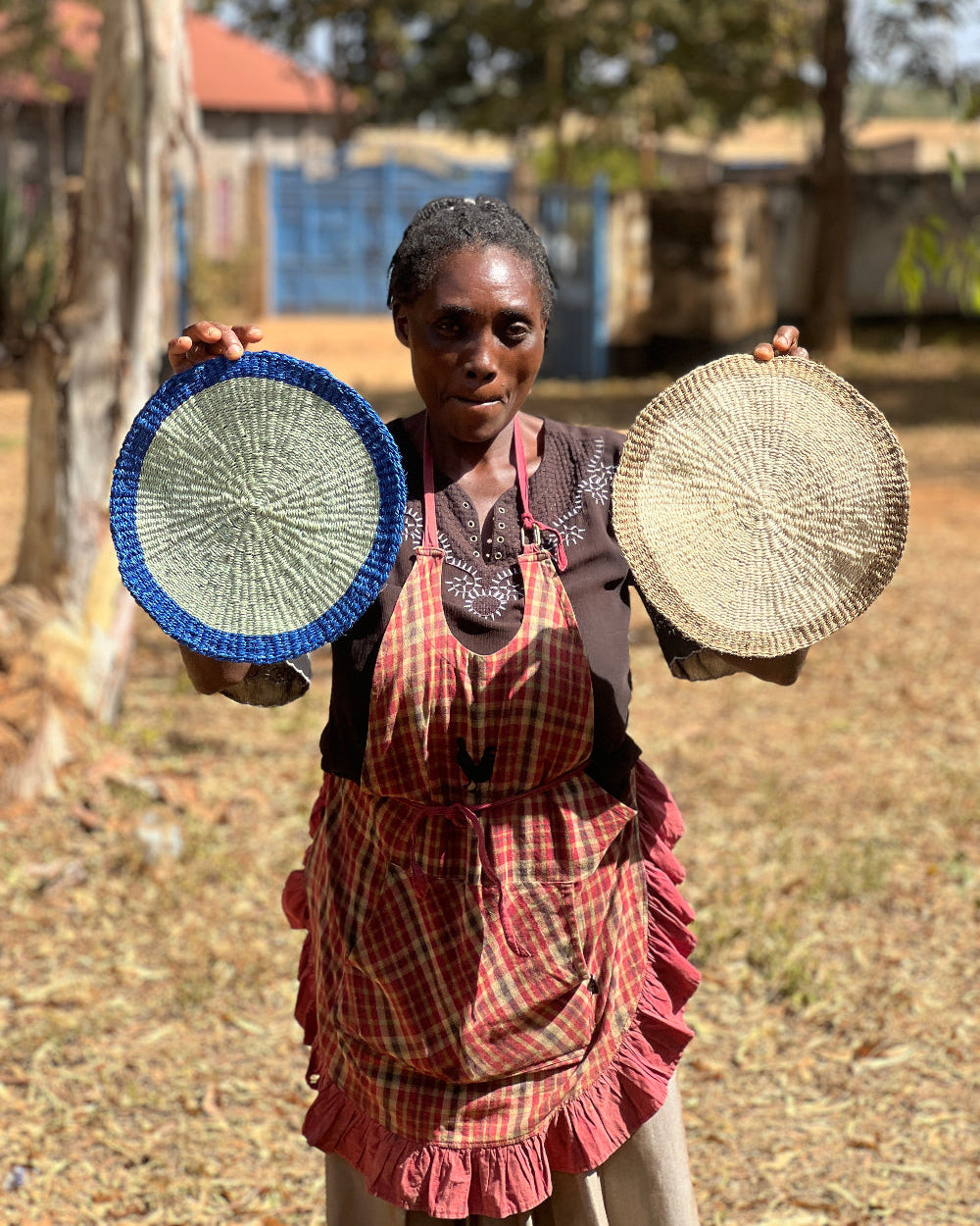 Woman holding two woven placemats outdoors in Kenya