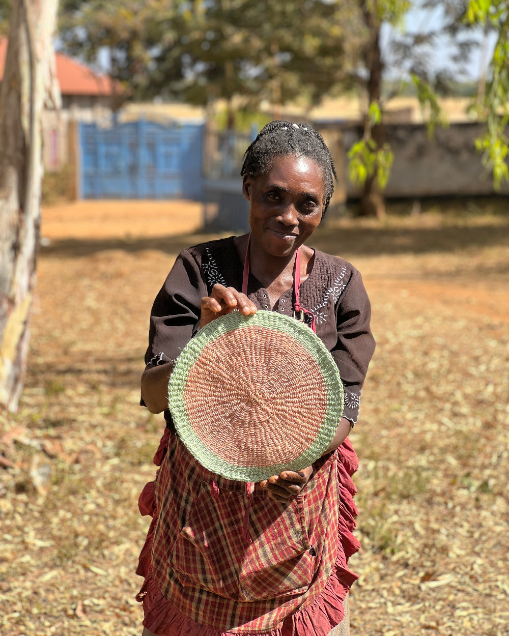 Woman holding a woven basket outdoors with trees and a blue container in the background.