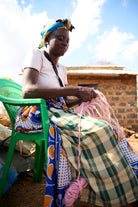 Woman sitting on a green chair, weaving with pink sisal outdoors.