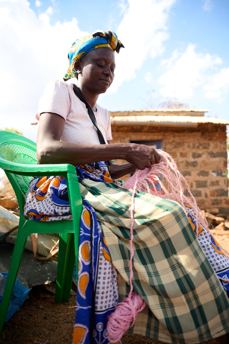 Woman sitting on a green chair, weaving with pink sisal outdoors.