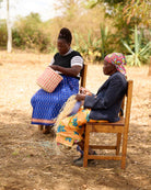Two women sitting outdoors, one weaving, with a natural background